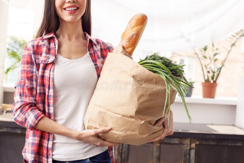 Junges Mädchen Lebensstilstellungs-Holdingtasche der Küche an der gesunden mit Stangenbrot und positiver Nahaufnahme des Gemüses lizenzfreie stockbilder Junges Mädchen Lebensstilstellungs-Holdingtasche der Küche an der gesunden mit Stangenbrot und positiver Nahaufnahme des Gemüses lizenzfreie stockbilder