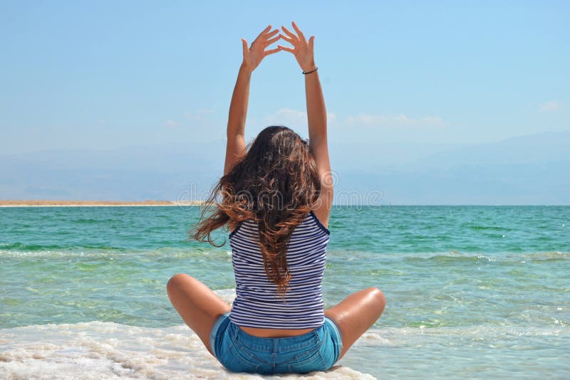 Junges Mädchen sitzt auf dem Ufer des Toten Meers in Israel, Ansicht von hinten der Brunette dehnt ihre Arme oben aus lizenzfreie stockfotos Junges Mädchen sitzt auf dem Ufer des Toten Meers in Israel, Ansicht von hinten der Brunette dehnt ihre Arme oben aus lizenzfreie stockfotos