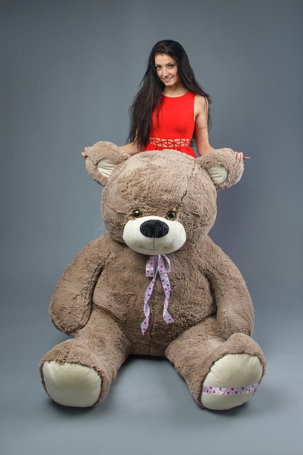 Junges schönes Mädchen im roten Kleid mit dem glücklichen Lächeln des großen Spielzeugs des Teddybären weichen und dem Spielen au stockfotografie Junges schönes Mädchen im roten Kleid mit dem glücklichen Lächeln des großen Spielzeugs des Teddybären weichen und dem Spielen au stockfotografie