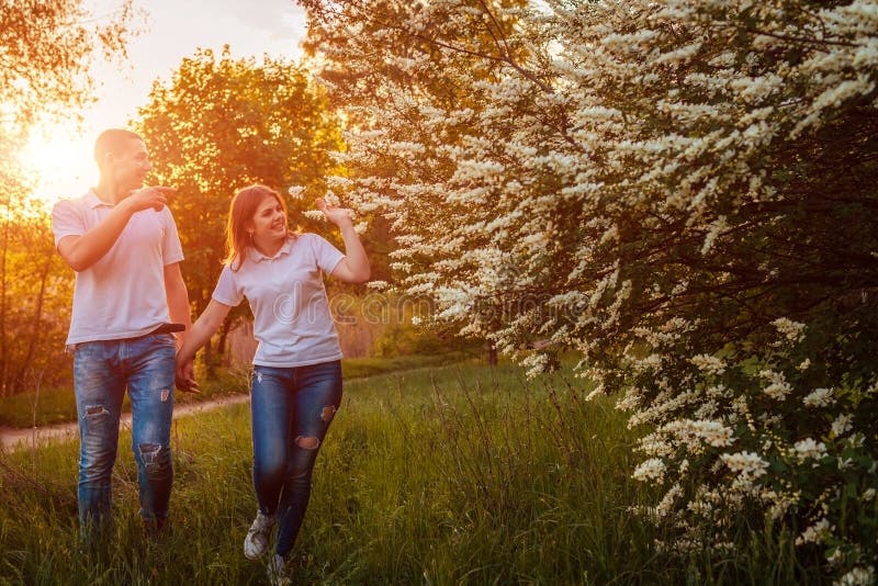 Junte caminar en parque floreciente de la primavera en la puesta del sol Hombre joven y mujer que tienen buen tiempo junto fotografía de archivo Junte caminar en parque floreciente de la primavera en la puesta del sol Hombre joven y mujer que tienen buen tiempo junto fotografía de archivo