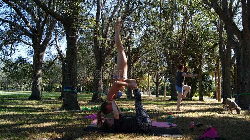 JUPITER, FLORIDA USA - 17. JUNI 2017 Junge Frauen, die acro Yoga u. slackline auf einem allgemeinen Park in Florida tun lizenzfreie stockbilder JUPITER, FLORIDA USA - 17. JUNI 2017 Junge Frauen, die acro Yoga u. slackline auf einem allgemeinen Park in Florida tun lizenzfreie stockbilder