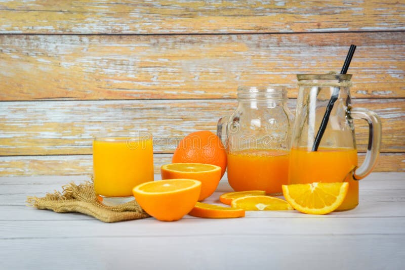 Jus d'orange dans la pot en verre et tranches de fruits frais à l'orange sur la table en bois - Jus de verre à vie sur fond de bo images stock Jus d'orange dans la pot en verre et tranches de fruits frais à l'orange sur la table en bois - Jus de verre à vie sur fond de bo images stock
