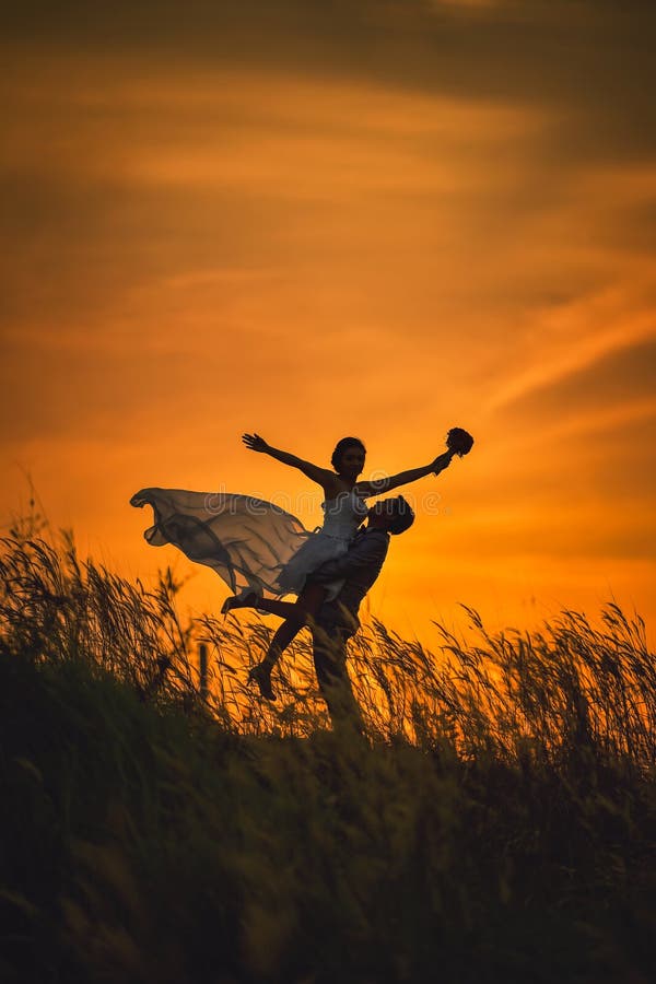 Just married loving hipster couple in wedding dress and suit on field at sunset