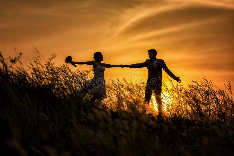 Just married loving hipster couple in wedding dress and suit on field at sunset