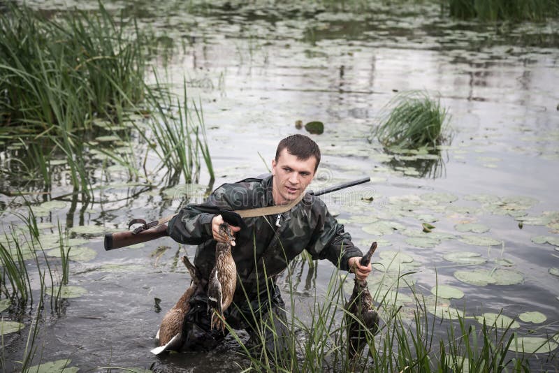 Jägermann mit Opfer nach einem erfolgreichen Jagdbruch durch Marschland lizenzfreie stockbilder Jägermann mit Opfer nach einem erfolgreichen Jagdbruch durch Marschland lizenzfreie stockbilder
