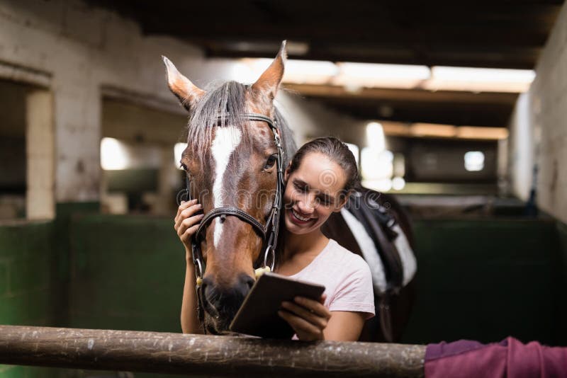 Jóquei fêmea de sorriso que usa a tabuleta digital ao estar pelo cavalo fotos de stock Jóquei fêmea de sorriso que usa a tabuleta digital ao estar pelo cavalo fotos de stock