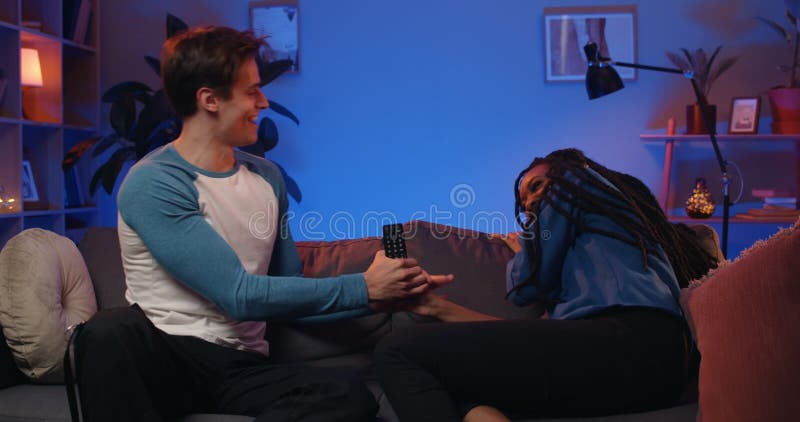 Jóvenes adultos alegres riéndose y peleando por control remoto en casa. novia milenaria y novio sonriendo y almacen de video