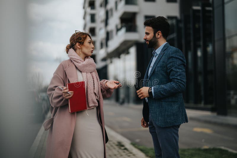 Two young professionals engaged in a business discussion outdoors, with city buildings in the backdrop. Two young professionals engaged in a business discussion outdoors, with city buildings in the backdrop.