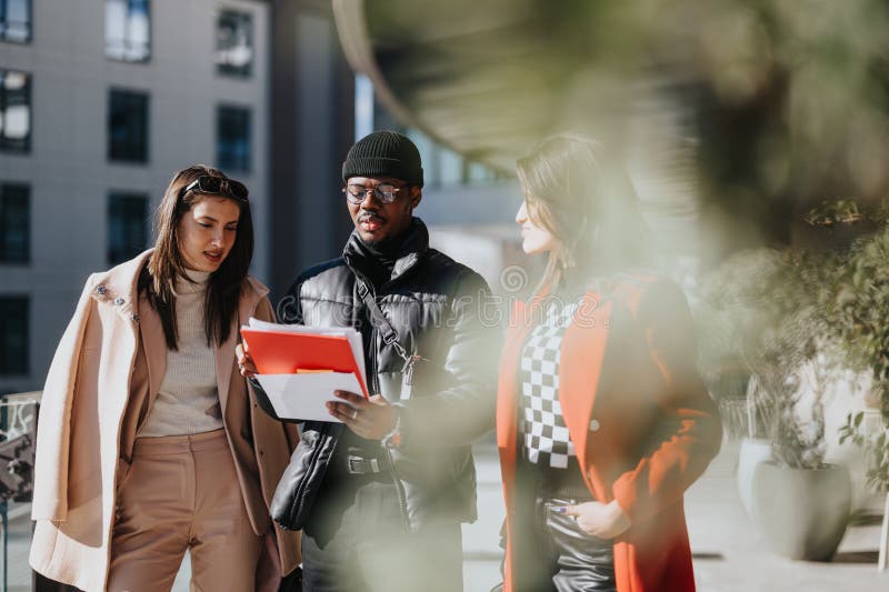 Three colleagues in stylish winter attire engage in a business meeting outside an office building, reviewing documents on a sunny day. Three colleagues in stylish winter attire engage in a business meeting outside an office building, reviewing documents on a sunny day.