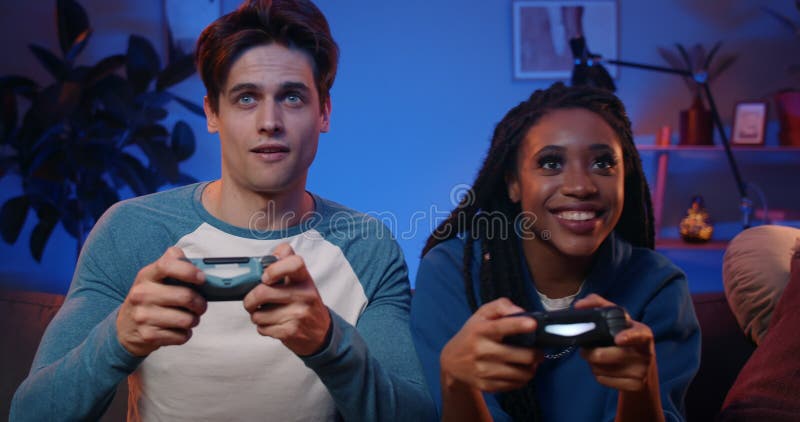 Jóvenes felices jugando videojuegos en la consola mientras están sentados en el sofá frente a la televisión. pareja milenaria pasa metrajes