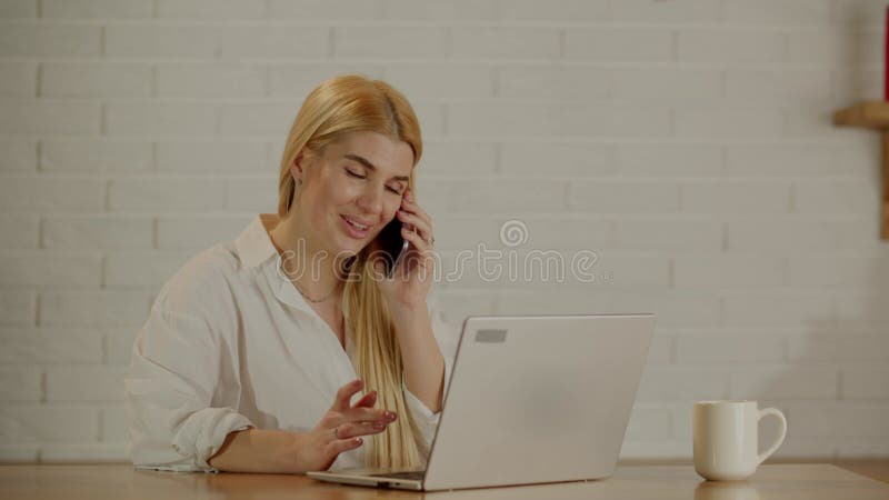 Jóvenes freelance enfocadas con ropa informal hablando en smartphone mientras trabajaban en proyectos remotos en laptop en almacen de video