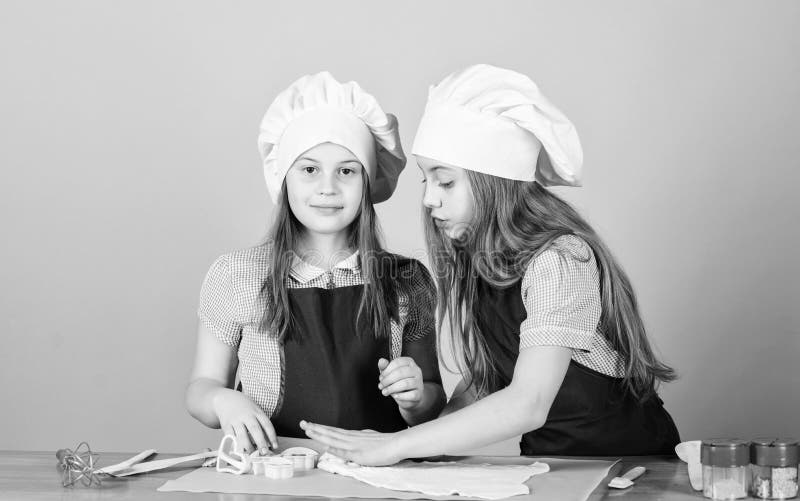 Jóvenes panaderos que siguen la receta de hornear Pequeños panaderos con pasta rodante en mesa de cocina Niñas horneando galletas fotografía de archivo Jóvenes panaderos que siguen la receta de hornear Pequeños panaderos con pasta rodante en mesa de cocina Niñas horneando galletas fotografía de archivo