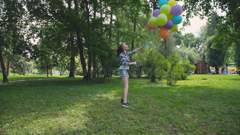 Júbilo feliz de la chica joven y giro con los globos coloridos en un parque metrajes