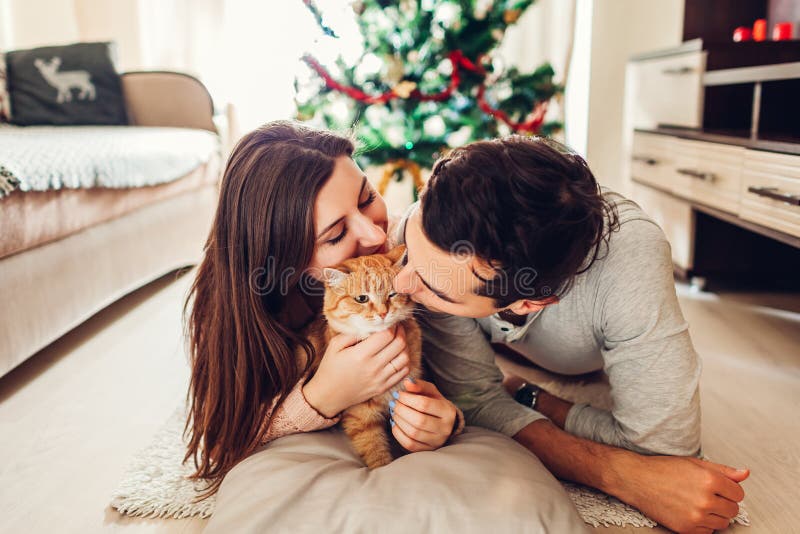 Júntese en el amor que miente por el árbol de navidad y que juega con el gato en casa Hombre y mujer que se relajan foto de archivo libre de regalías Júntese en el amor que miente por el árbol de navidad y que juega con el gato en casa Hombre y mujer que se relajan foto de archivo libre de regalías