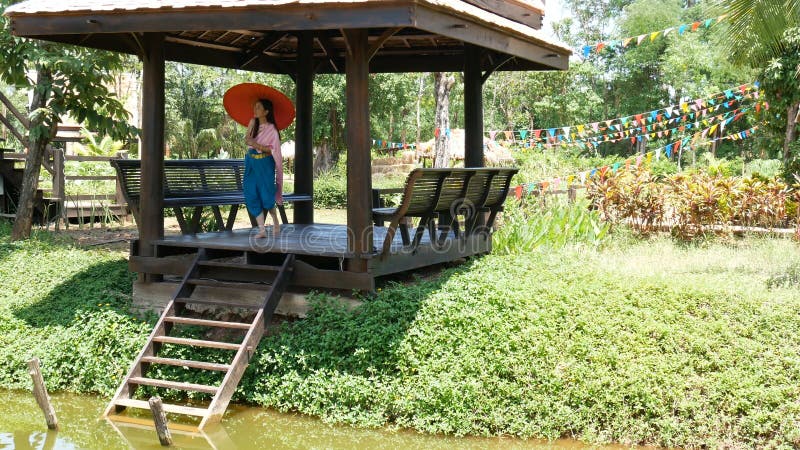 4K härlig thailändsk traditionell dräkt för kvinnakläder av Thailand med det röda paraplyet som går i thailändsk sala på flodstra