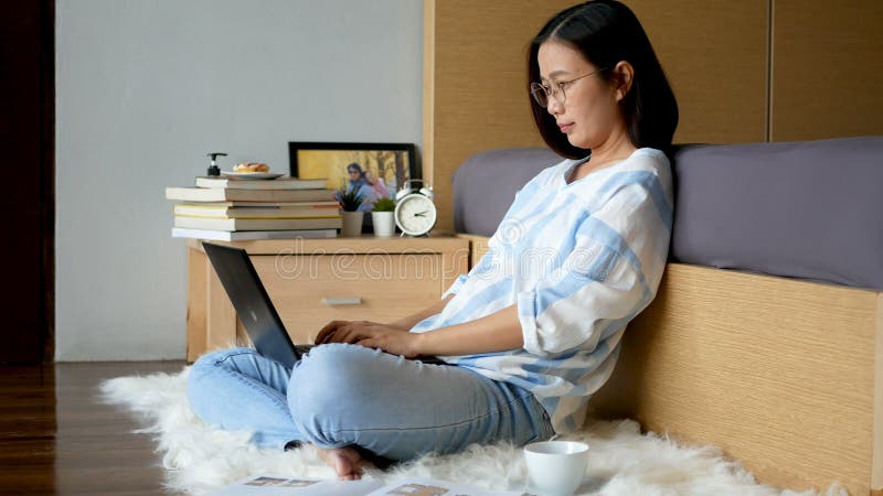 4k. lavoro domestico. donna che digita sulla tastiera lavorando con computer portatile sul pavimento in camera da letto durante l' stock footage
