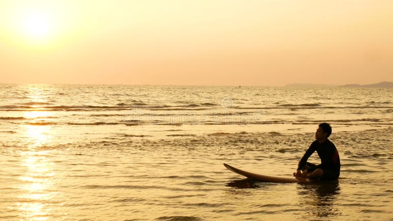 4K Schattenbild des Surfermannes entspannen sich, indem es auf Surfbrett über dem Meer bei Sonnenuntergang auf tropischem Strand