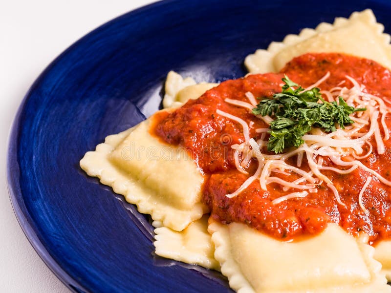A close-up view of a dish of homemade cheese ravioli topped with a tomato sauce, shredded cheese and parsely. A close-up view of a dish of homemade cheese ravioli topped with a tomato sauce, shredded cheese and parsely