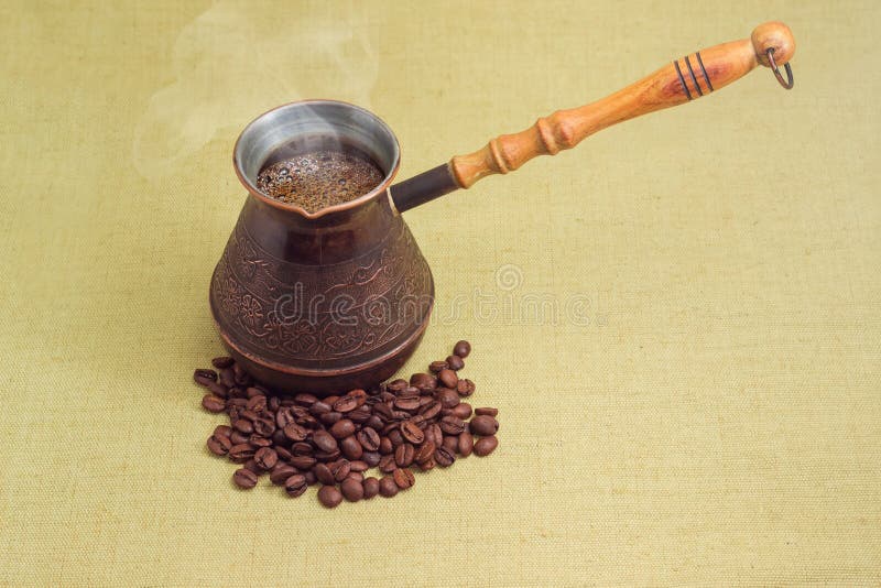 Kaffe i årgång, kopparkaffekanna och rostade kaffebönor. Svart rostat kaffe i en årgång kopparkaffekanna som är spridd på rostade kaffebönor bredvid textilytan