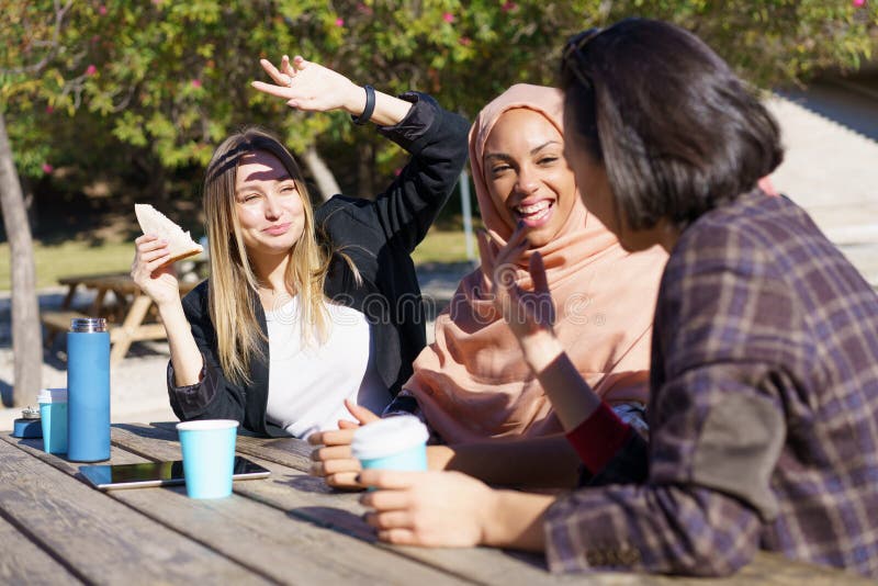 Kaffe och leende i parker, glada, kvinnliga vänner av flera etniska slag. arkivbilder