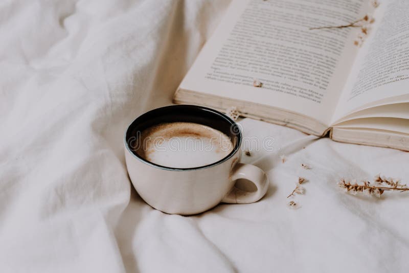 Cozy coffee on the bed with white bed sheets and an old book on the background. Warm tones. Relaxing moment concept. Detail. Cozy coffee on the bed with white bed sheets and an old book on the background. Warm tones. Relaxing moment concept. Detail