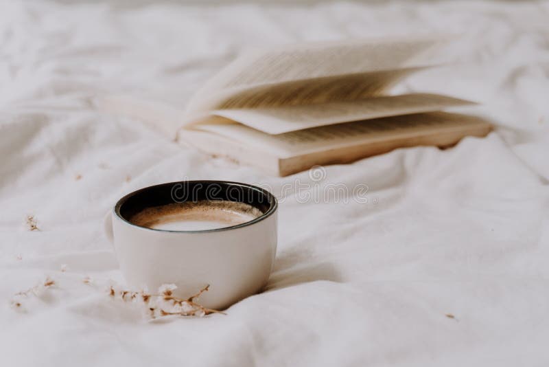 Cozy coffee on the bed with white bed sheets and an old book on the background. Warm tones. Relaxing moment concept. Selective focus. Cozy coffee on the bed with white bed sheets and an old book on the background. Warm tones. Relaxing moment concept. Selective focus.