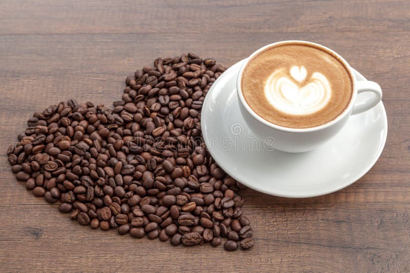 Kaffekopp av lattekonst med kaffebönor i hjärtaform på trä royaltyfri bild