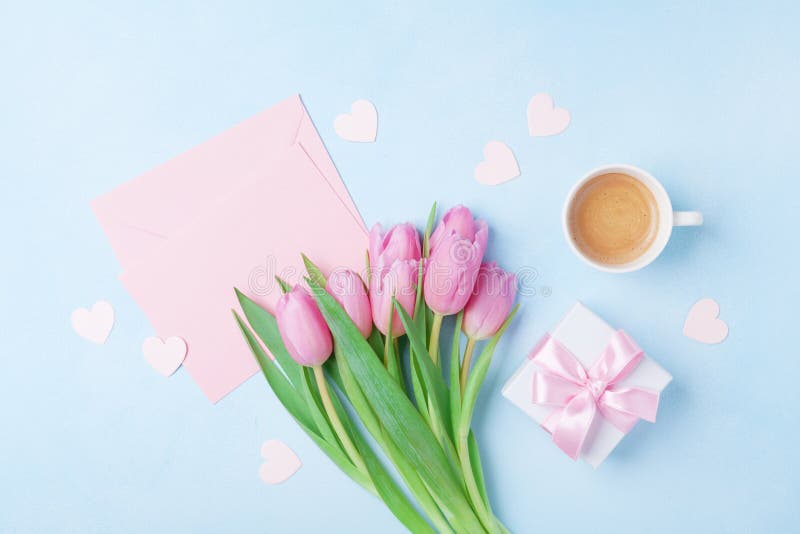 Kaffekopp, vårtulpanblommor, gåvaask och rosa pappers- kort på blå pastellfärgad bästa sikt för tabell Hälsning för kvinnas eller