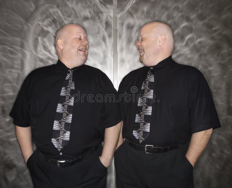 Caucasian bald mid adult identical twin men looking at each other laughing. Caucasian bald mid adult identical twin men looking at each other laughing.