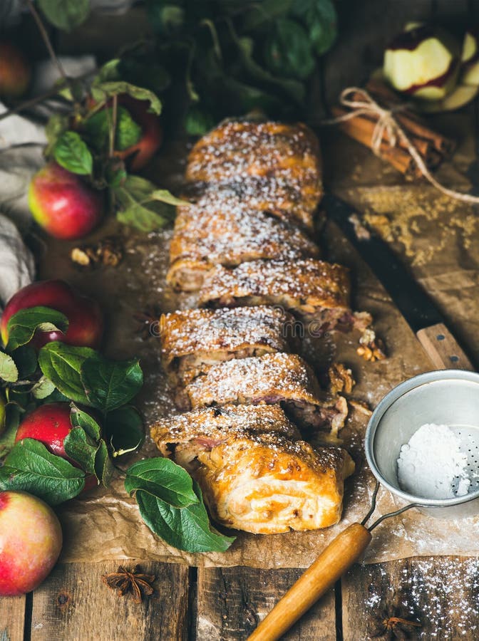 Apple strudel cake with cinnamon, sugar powder and fresh apples on rustic wooden table background, selective focus, vertical composition. Apple strudel cake with cinnamon, sugar powder and fresh apples on rustic wooden table background, selective focus, vertical composition