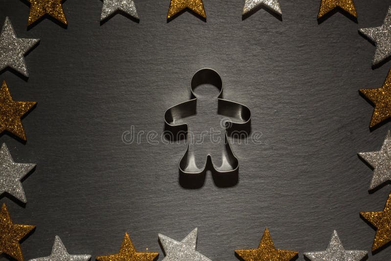 Cookie cutter for gingerbread man on slate background with frame of golden and silver stars, Christmas decoration. Cookie cutter for gingerbread man on slate background with frame of golden and silver stars, Christmas decoration.