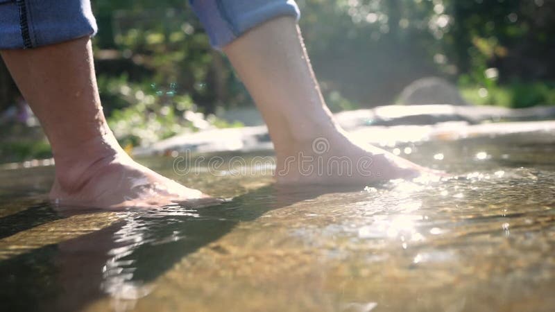 Kale voeten jonge vrouw die haar benen in het water spuwt en schoppen in de stroom die langzaam stroomt. dames genieten van vakant