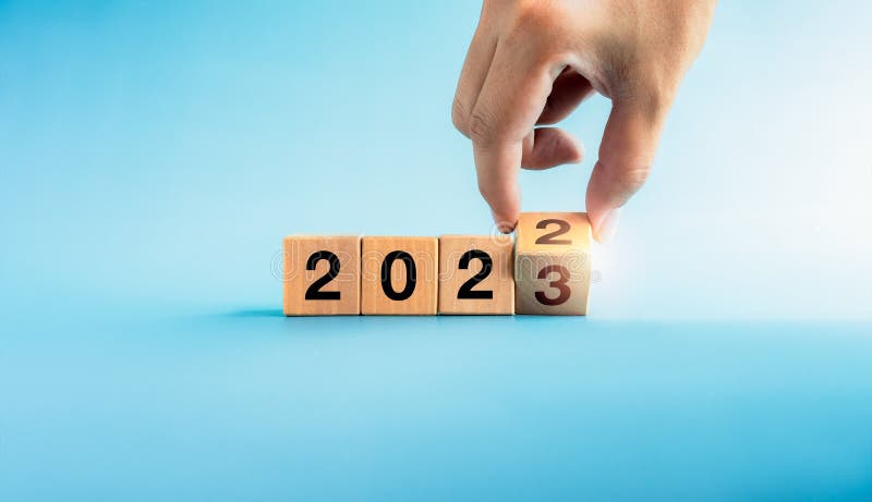 The calendar year 2022 changed to the new year 2022. Close-up hand turning number 2 to 3 on wooden the last cube block for the transition from 2022 to 2023 isolated on blue background, ready to begin. The calendar year 2022 changed to the new year 2022. Close-up hand turning number 2 to 3 on wooden the last cube block for the transition from 2022 to 2023 isolated on blue background, ready to begin.