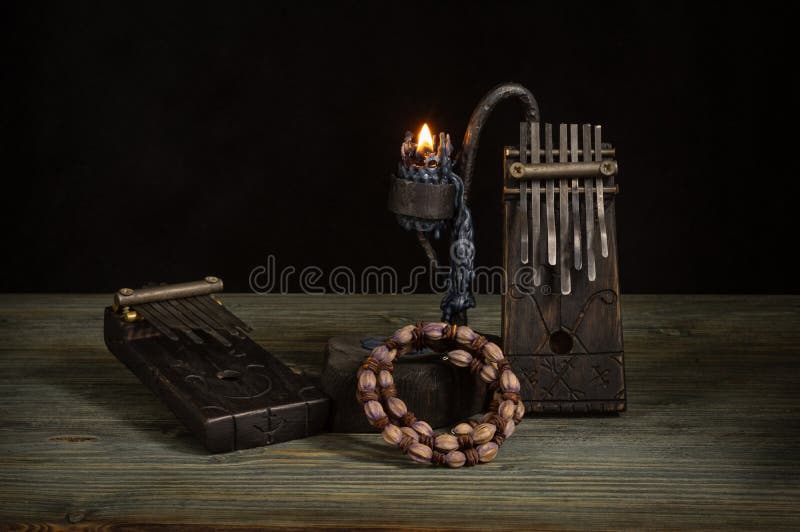 A Kalimba musical instrument made of dark wood with a geometric pattern, a candle holder with a burning candle and an African wome