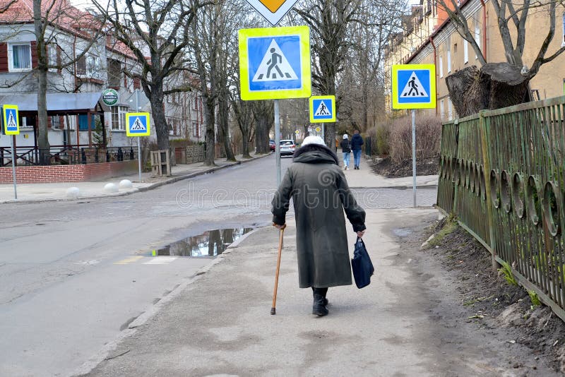 KALININGRAD, RUSSIA. Hunched old woman walks down Kommunalnaya street in early spring