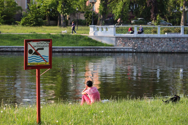 Kaliningrado, Rusia - 1 de junio de 2019: Mujer que se sienta en la costa del lago de la ciudad foto de archivo Kaliningrado, Rusia - 1 de junio de 2019: Mujer que se sienta en la costa del lago de la ciudad foto de archivo