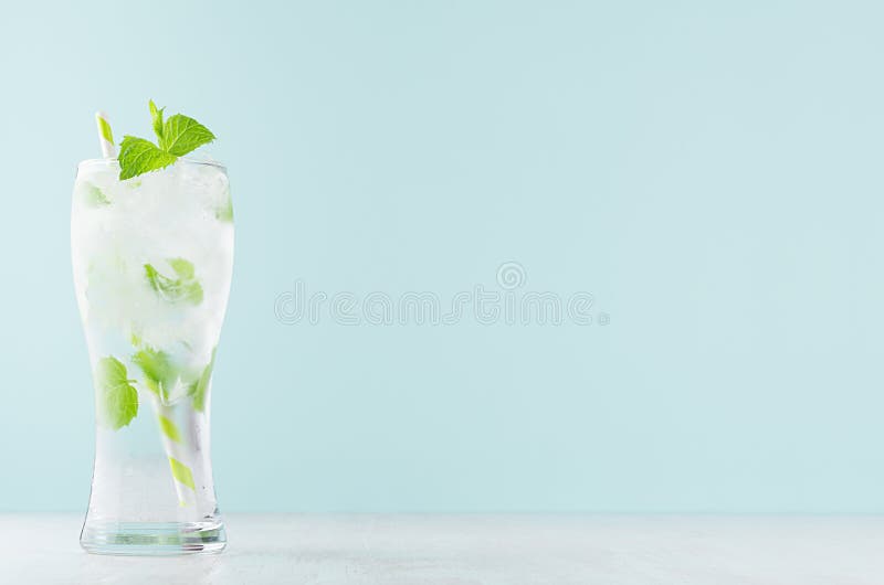 Kall ljus organisk coctail med den gröna mintkaramellen, iskuber, uppiggningsmedel, sugrör i ljus mjuk pastellfärgad blå färgbakg