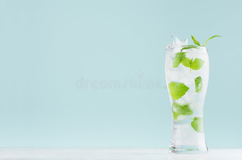Kall mintkaramelldrink för ny sommar med det gröna bladet, iskuber, uppiggningsmedel i ljus mjuk pastellfärgad blå färgbakgrund p