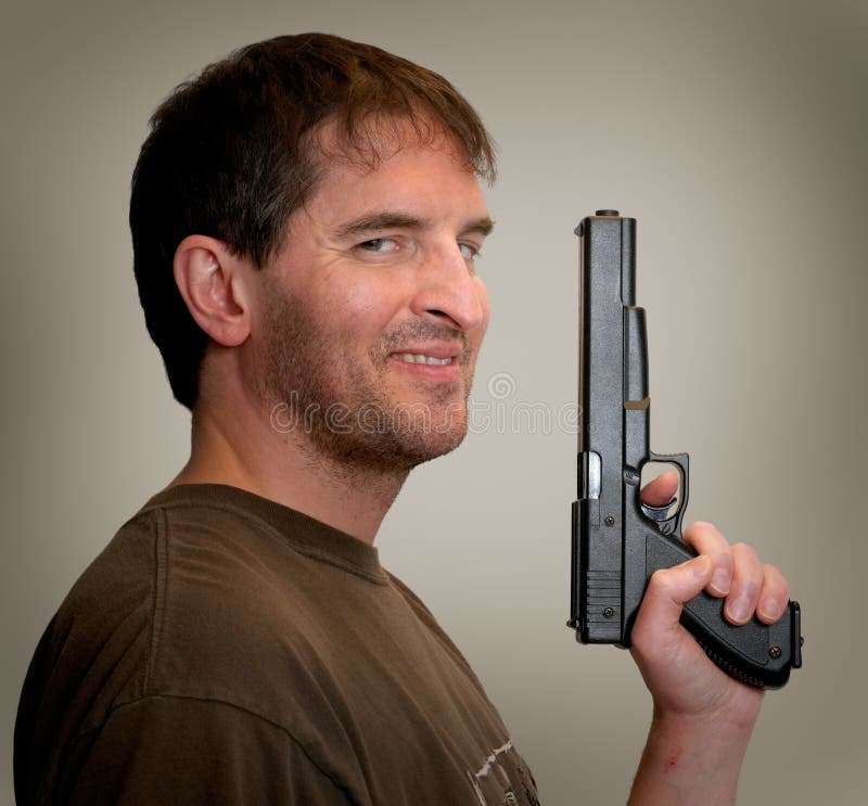 Smiling, slightly crazy-looking man looking sidelong at camera, holding gun up in front of him. Smiling, slightly crazy-looking man looking sidelong at camera, holding gun up in front of him.