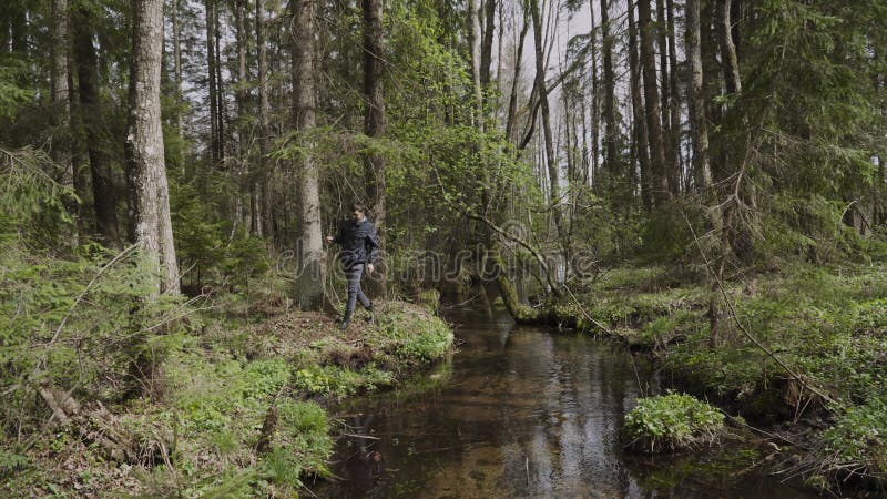 Kalmerende man in rubberlaarzen neemt een stap langs de oever in de buurt van een heldere beek in het bos.