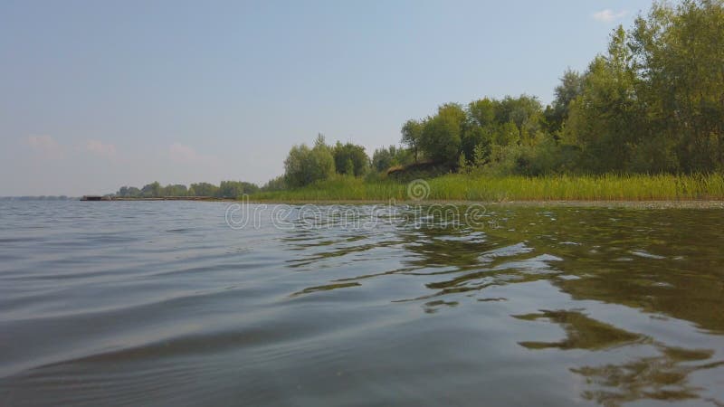 Kamera porusza się nad wodą dużej rzeki, na której brzegu znajduje się las