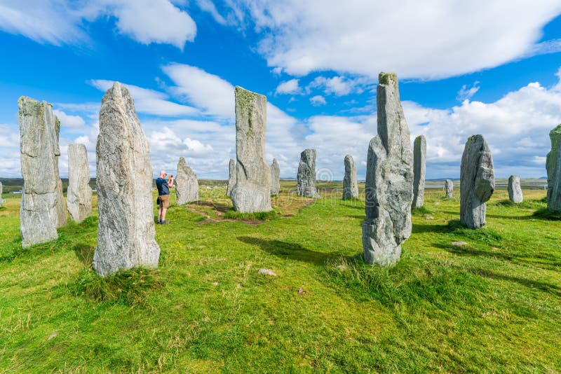 CALLANISH, ISLE OF LEWIS, SCOTLAND - AUGUST 03, 2022: Tourists visit Callanish standing stones site on the Isle of Lewis. The stones were erected in the late Neolithic era. CALLANISH, ISLE OF LEWIS, SCOTLAND - AUGUST 03, 2022: Tourists visit Callanish standing stones site on the Isle of Lewis. The stones were erected in the late Neolithic era