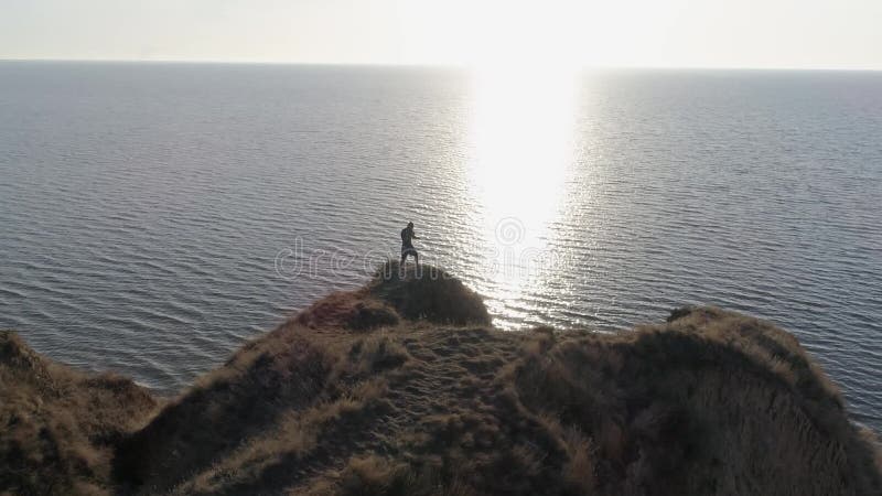 Kampsporter i det härliga landskapet, idrottsman kopplade in Kickboxing på kullen vid havet i ljust solljus på vatten mot himmel