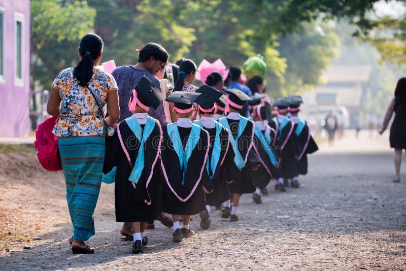 Kanchanaburi Thailand, Mar 6, 2020: Asian kids boys and girls graduate walking in a line with parents. Children wore black robes, had blue and pink stripes, and they wore hats for graduates. Kanchanaburi Thailand, Mar 6, 2020: Asian kids boys and girls graduate walking in a line with parents. Children wore black robes, had blue and pink stripes, and they wore hats for graduates.