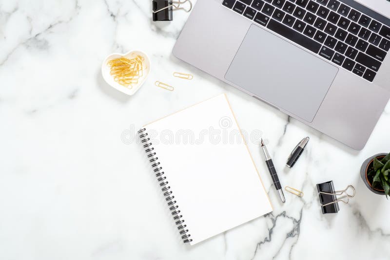 Office desk table with laptop computer, blank paper notepad, stationery, succulent plant on white marble surface. Flat lay, top view feminine background. Business woman workspace. Office desk table with laptop computer, blank paper notepad, stationery, succulent plant on white marble surface. Flat lay, top view feminine background. Business woman workspace