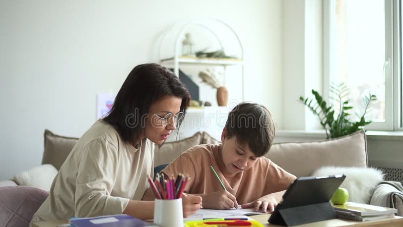 Karantän för hemfolk : Mamma son skriver eller ritar vid bordet med en tablett i rumsformat. lager videofilmer