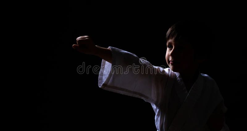 Karate chłopiec w białym kimonie pozuje na ciemnym tle Dziecko gotowy dla sztuka samoobrony walki Dzieciaka bój przy Aikido szkol