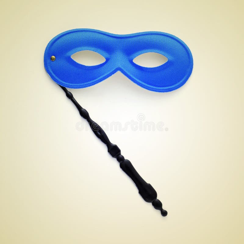 Picture of a handled blue carnival mask on a beige background, with a retro effect. Picture of a handled blue carnival mask on a beige background, with a retro effect