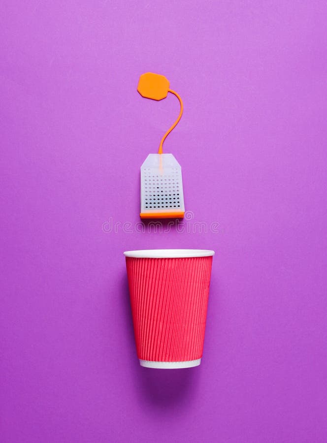 Cardboard tea cup and teabag on purple background. Top view. Minimalism. Cardboard tea cup and teabag on purple background. Top view. Minimalism