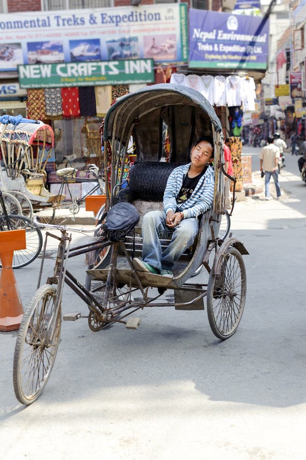 KATMANDU NEPAL - MAJ 17, 2014: Trött chaufför för cirkuleringsrickshaw som sover på hans medel på ingången av Thamel område Katma arkivbild KATMANDU NEPAL - MAJ 17, 2014: Trött chaufför för cirkuleringsrickshaw som sover på hans medel på ingången av Thamel område Katma arkivbild